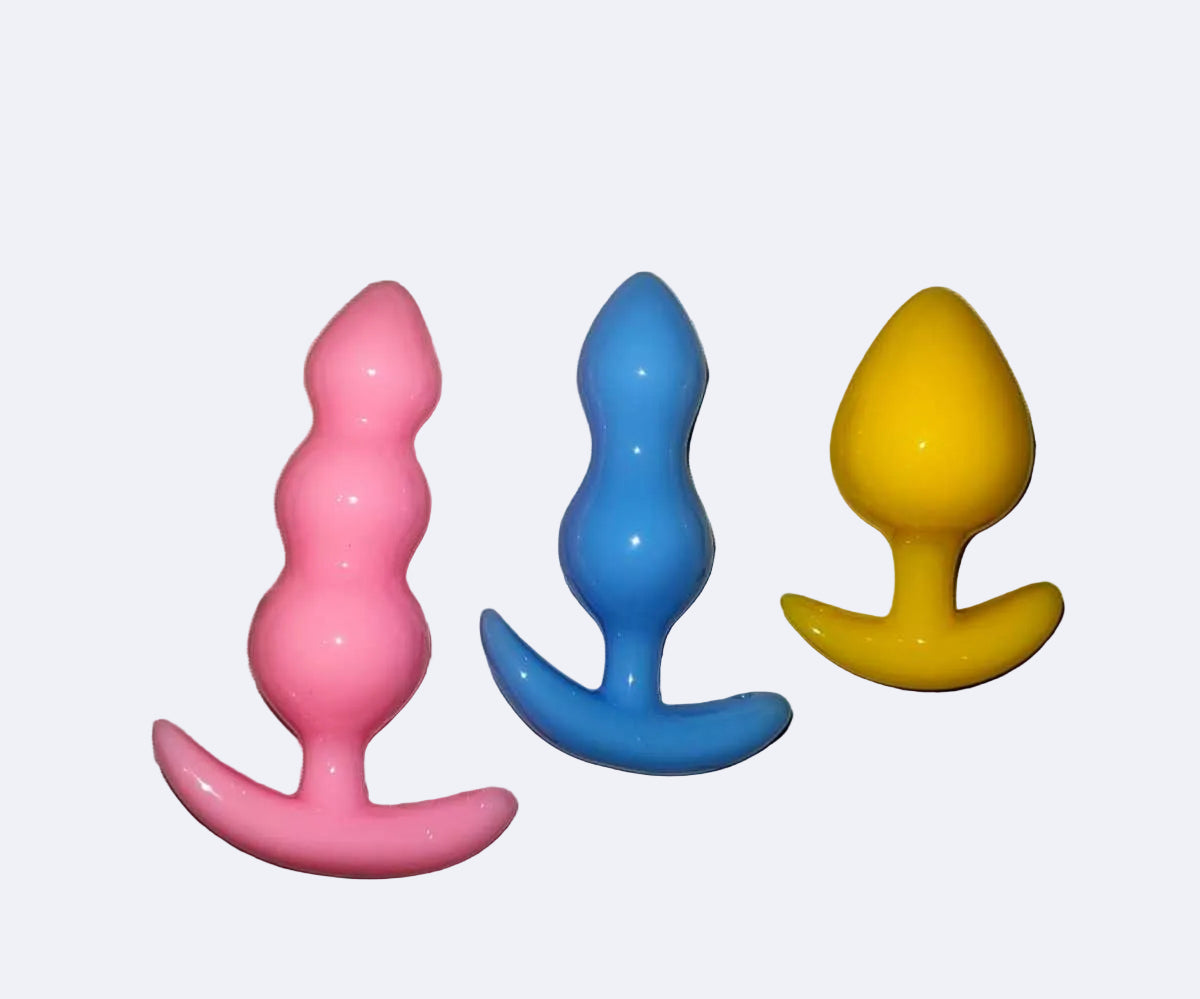 Three colorful silicone butt plugs on a light fabric background